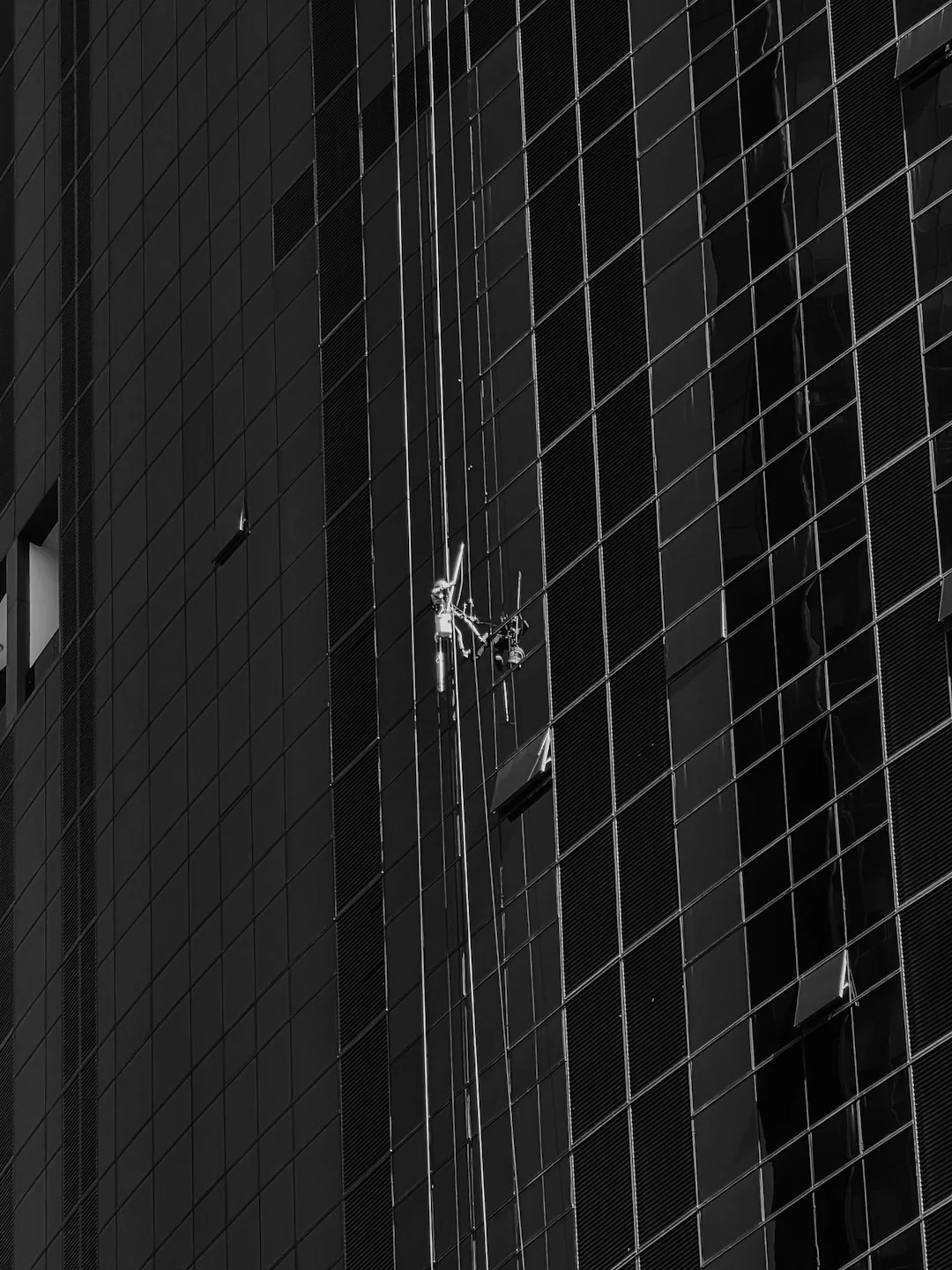 Three window cleaners suspended on ropes clean a modern glass building facade during the day.