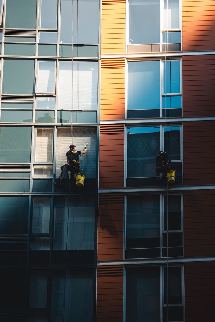 Two workers suspended while cleaning windows on the facade of a modern skyscraper.