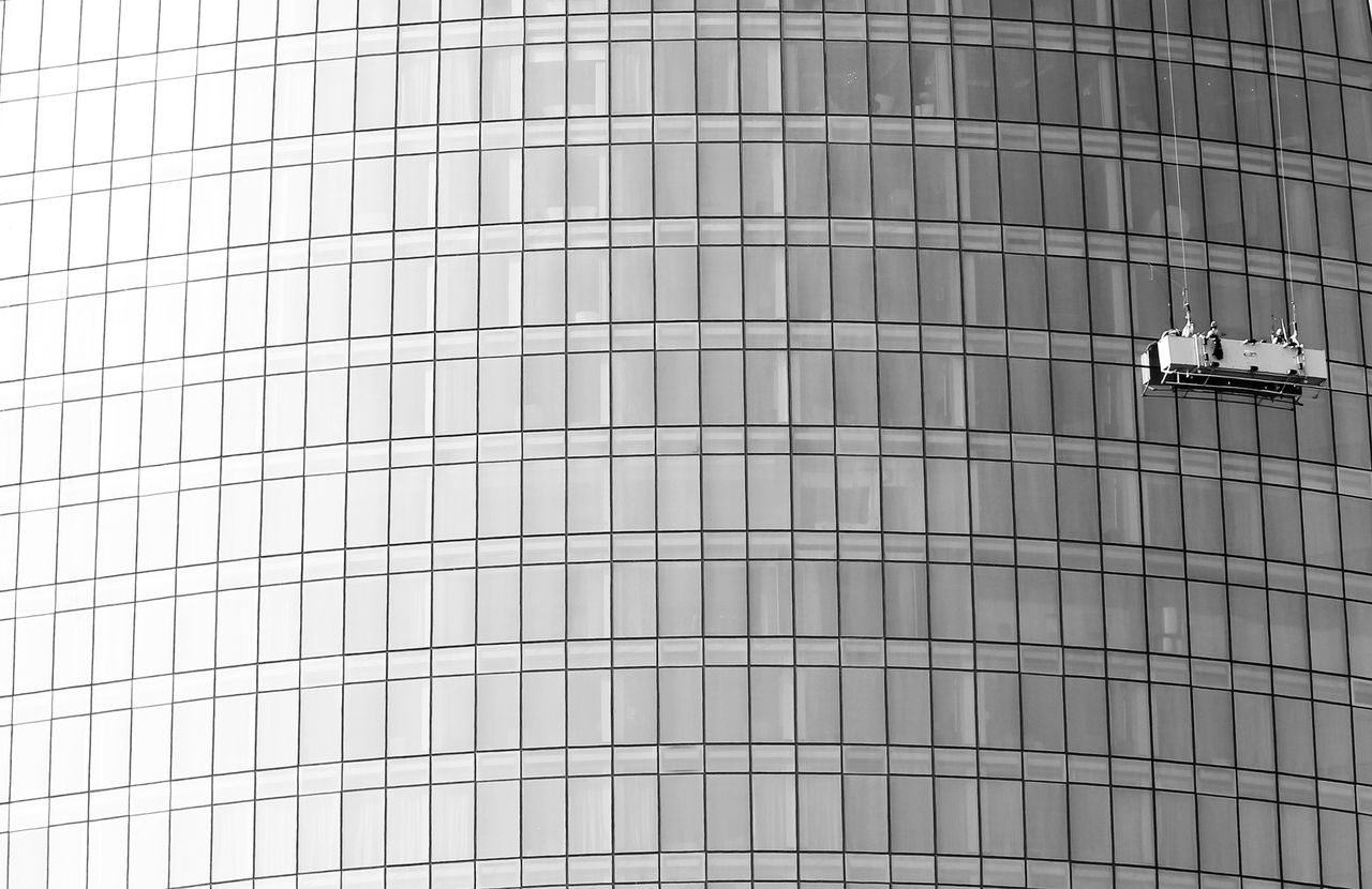 Façade vitrée d’un immeuble de grande hauteur avec une plateforme suspendue pour le nettoyage des fenêtres.